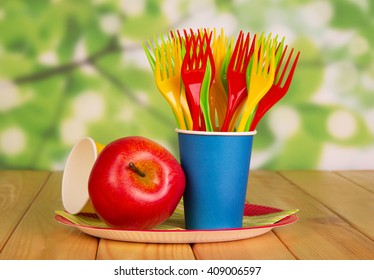 Bright disposable tableware and apple on an abstract green background.