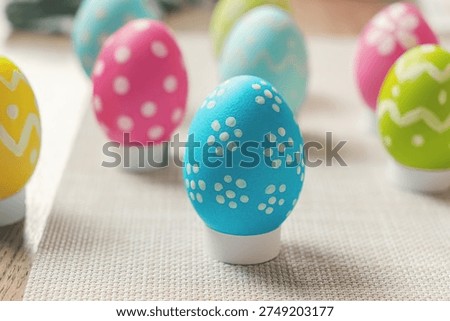 Bright Easter eggs in blue, pink, green, and yellow are placed on a gray napkin and decorated with playful patterns. Each egg has a unique design of dots and zigzags. Photo