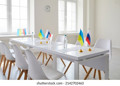 Bright Empty Meeting Room For Talks Between Representatives Of Ukraine And Russia. Empty Chairs At White Table With State Flags, Documents And Bottles Of Water. Concept Of Negotiations To End War.