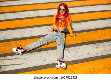 Bright Exciting Girl With Red Hair, 90s, 2000s Style, T-shirt, Wide Jeans, Bananas, Sneakers. Sitting At A Pedestrian Crossing