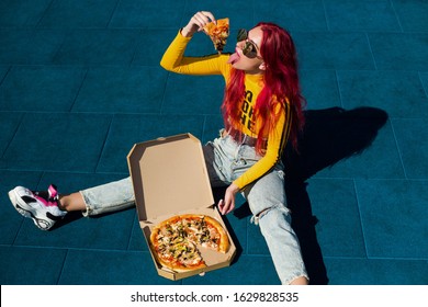 Bright Exciting Girl With Red Hair, Style Of The 90s, 2000s, Jacket, Wide Jeans, Bananas, Sneakers. Eats Pizza Out Of The Box On A Basketball Court In Summer