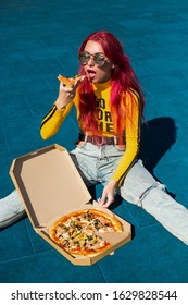 Bright Exciting Girl With Red Hair, Style Of The 90s, 2000s, Jacket, Wide Jeans, Bananas, Sneakers. Eats Pizza Out Of The Box On A Basketball Court In Summer