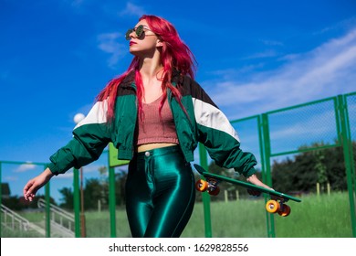 Bright Exciting Girl With Red Hair, Style Of The 90s, 2000s, Jacket, Leggings, Sneakers. On A Basketball Court In The Summer In The Hands Of A Ball, A Skateboard