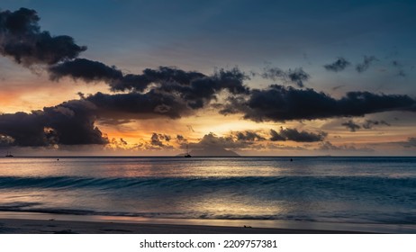 A bright fantastic sunset on a tropical island. The sky is highlighted in orange and pink. Dark blue clouds. A wave rolls onto the beach. Reflection. Long exposure. Seychelles. Mahe. Beau Vallon - Shutterstock ID 2209757381