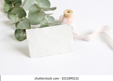Bright feminine spring stationery mockup scene with a handmade paper greeting card, spool of silk ribbon and eucalyptus leaves on a white table background. Wedding styled stock photography. - Shutterstock ID 1011890131