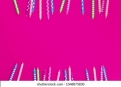 Bright festive candles in two rows as border on trendy fucsia background in flat lay with copy space. Greeting happy birthday feminine girlie celebration card or party invitation