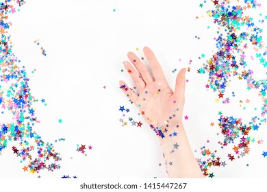 Bright festive color confetti star sparkles with woman hand on white background. Creative conceptual Christmas holiday birthday party top view flat lay backdrop for your blog, text or design