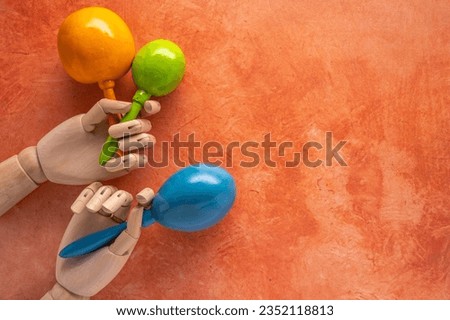 bright festive musical theme with yellow, green and blue maracas in wooden hands on a mottled orange background