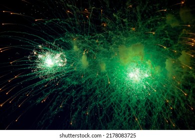 A bright firework with a green glowing center with orange sparks flying towards the background of the night sky. High quality photo