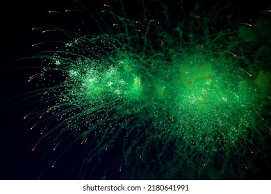 A bright firework with a green glowing center with orange sparks flying towards the background of the night sky. High quality photo