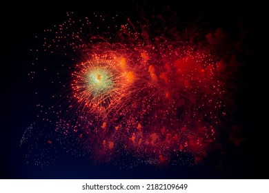 A bright firework with a green glowing center and red sparks and smoke flying towards the background of the night sky. High quality photo