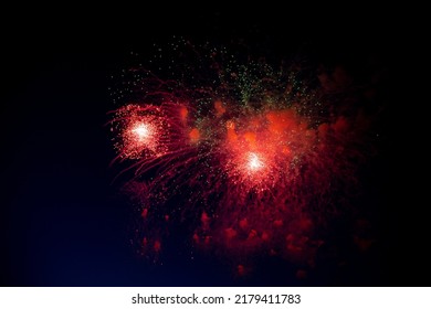 A bright firework with a red glowing center with red and green sparks and smoke flying towards the background of the night sky. High quality photo