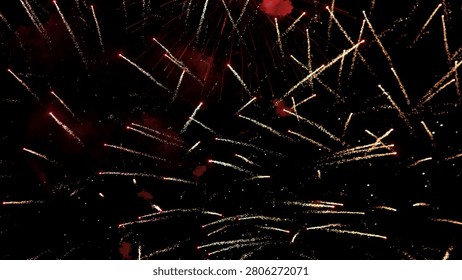 Bright fireworks explode across dark night sky with golden spark trails, red glowing smoke and scattered flashes, creating lively festive celebration scene with vivid contrast