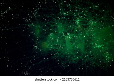 Bright fireworks with a green glowing center with green sparks and smoke flying towards the background of the night sky. High quality photo