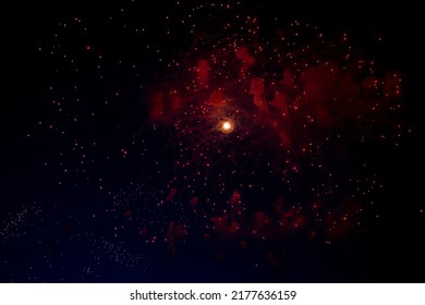 A bright flash in the center from the fireworks beginning to bloom and red sparks around against the background of the night sky. High quality photo