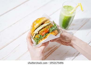 Bright Fresh Veggie Burger Without Gluten And Meat. Woman Eating Vegan Burger In A Restaurant And Drinking Green Smoothie
