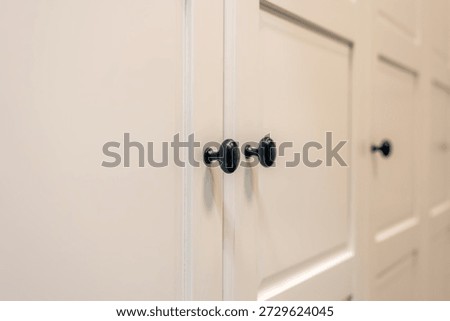 Bright fronts with black knobs lead into depth and suggest a smart storage system. Soft focus and neutral tones match clean home and minimal interior trends.