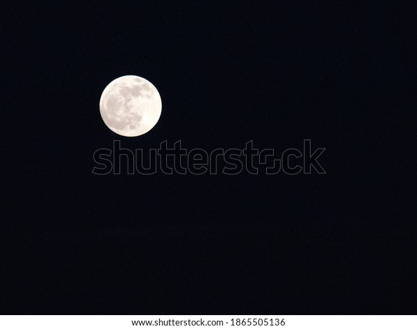Bright full moon is rising up to illuminate a black\
night sky.