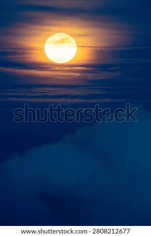 Bright full moon shining through thin clouds in a deep blue evening sky. Atmospheric night sky scene with detailed lunar surface, soft cloud formations, and a tranquil celestial landscape ideal for astronomy, nature, and background concepts.