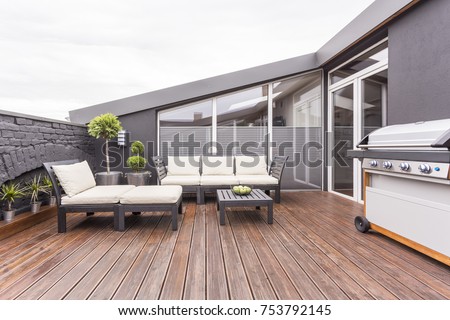 Bright garden furniture, grill and plants on cozy terrace with wooden floor and brick wall