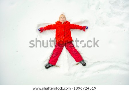 a bright girl in red clothes makes an angel in the snow lying top view on a winter day