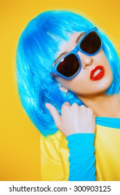 Bright glamorous girl in vivid clothes and a wig alluring over yellow background. Beauty, fashion. Cosmetics, hairtsyle. Optics, eyewear.