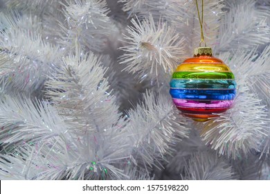 Bright glass rainbow colored Christmas ball  bauble hanging white artificial christmas tree  The concept the holiday  Christmas  symbol the rainbow  Copy space