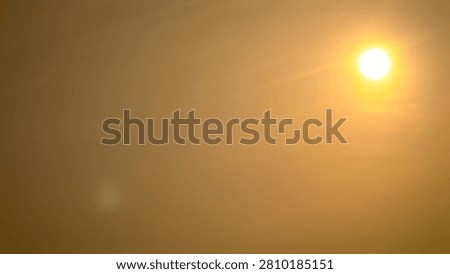 Bright glowing sun shining through a hazy, warm orange and sepia sky