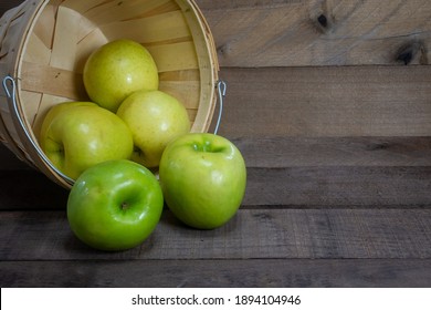 Bright Green Granny Smith Apples Spill Out Of A  Basket Onto Dark Wood.