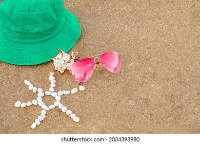 Bright Green Hat, Pink Glasses, Unusual Shell, Sun Laid Out With Small White Pebbles On Sand Beach, Copy Space. Concept Summer Beach Holiday In Hot Countries, Summer Holidays. Blank Packaging Layout.