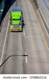 Bright Green Industrial Classic American Big Rig Semi Truck With Chrome Parts And Oversize Load Sign On The Front Bumper Transporting Cargo On Flat Bed Semi Trailer Running On The Overpass Road