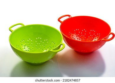 Bright Green And Orange Colored Plastic Colanders With Reflections On Shinny Counter Surface. High-angle View