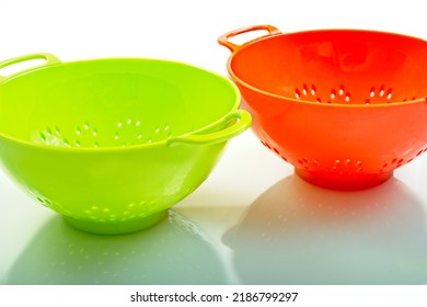 Bright Green And Orange Colored Plastic Colanders With Hazy Reflections On Shinny Counter Surface