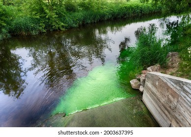 Bright Green Polluted Effluent Flowing Down A Concrete Spillway Into A Pristine Waterway Forming A Cloud Of Pollution In An Environmental And Ecological Concept