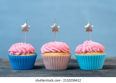Bright holiday card with three cupcakes and candles in the form of stars on blue background. Muffin with pink buttercream frosting