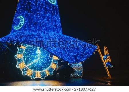 Bright holiday wizard hat light structure with glowing clock face and small climbing figure at night