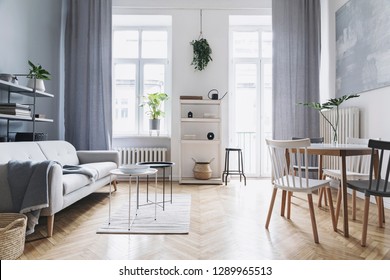 Bright Home Nordic Living Room With Design Sofa, Family Table, Plant, White Bookstand On The Wall. Brown Wooden Parquet. Abstract Painting On The White Wall.  Concept Of Minimalistic Interior.