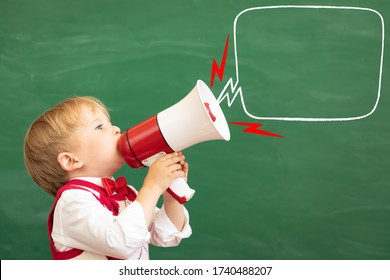 Bright Idea! Funny Child Student Speaking By Megaphone In Class. Happy Kid Shouting By Loudspeaker Against Green Chalkboard. Online Education And E-learning Concept. Back To School