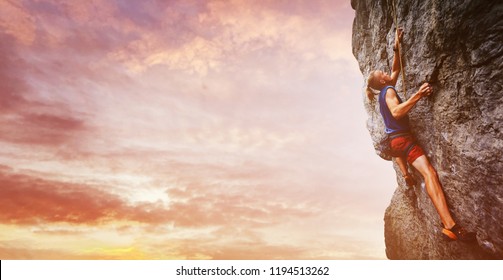 bright image of young man rock climber with long hair wearing in bright red shorts and blue t-shirt climbing the challenging route on the cliff. rock climber climbing on a limestone wall on the
