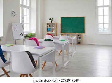 Bright interior of empty classroom without students in modern elementary school. School classroom with blackboard, white desks and chairs with colored backpacks. Educational concept. - Shutterstock ID 2192949349