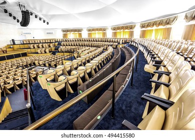 Bright interior of a modern concert hall with a stage and rows of comfortable leather chairs, a stage and acoustic amplification system under natural light, prepared for presentation