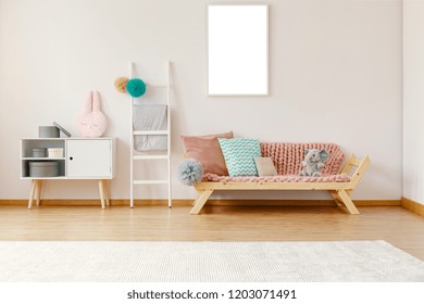 Bright Kid Room Interior With Wooden Couch With Powder Pink Coverlet, Cushions And Elephant, White Carpet On The Floor, Ladder With Pompoms And Mockup Poster On The Wall In The Real Photo