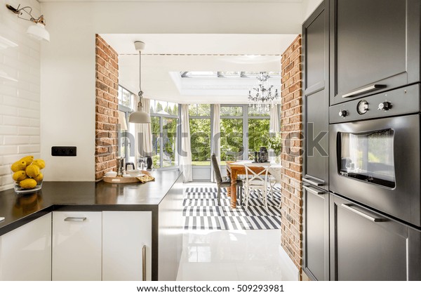 Bright\
kitchen area with modern amenities, close brick walls with the view\
of minimalistic dining room surrounded by\
windows