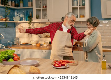 in bright kitchen an elderly man before cooking an elderly woman in a green shirt smiling from behind ties an apron for her husband a happy couple - Powered by Shutterstock