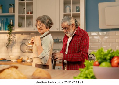 in bright kitchen an elderly man in a red shirt smiling from behind before cooking ties an apron for his wife a happy couple - Powered by Shutterstock