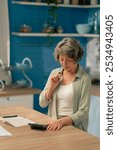 in bright kitchen an elderly woman in a light green shirt stands near a table with money counts savings hard old age finds funds