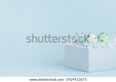 Bright and laconic easter background with blue eggs with golden dots in gift box on blue backdrop, closeup.