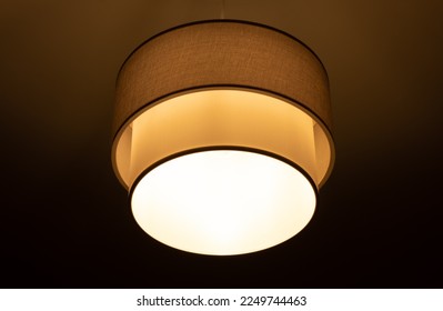 bright lamp burning in a round lampshade, lampshade lighting indoors on a dark background