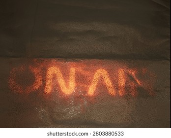 A bright light forms letters on a surface at night. The letters glow in orange color and stand out in the dark. The setting is likely a busy urban area.