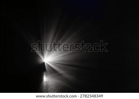 Bright light source projects rays into a dark environment, illuminating a reflective floor with dramatic shadows and highlights